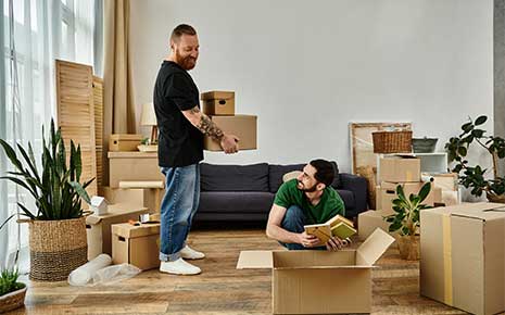 a gay couple in love, stand in a living room surrounded by moving boxes, starting a new chapter together.
